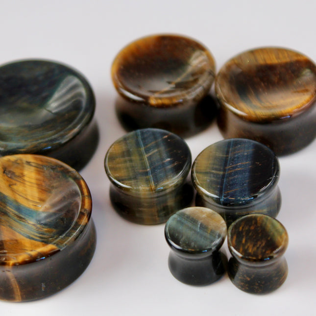 BLUE TIGERS A sleek and polished pair of Blue Tiger Eye plugs, also known as Falcon’s Eye, radiating deep shades of midnight blue, slate, and hints of black. Each plug features the signature chatoyancy of the stone—a silky, light-catching shimmer that moves across the surface as it shifts in the light. The smooth, double-flared design offers both comfort and style, with each plug showcasing natural banding and a unique pattern.