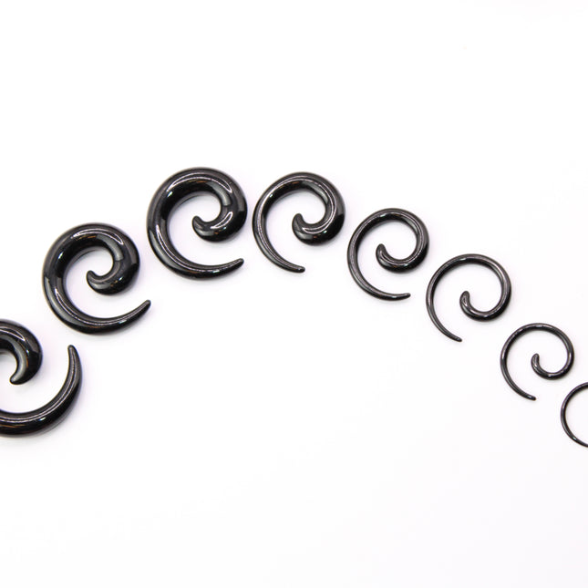 A pair of sleek, black acrylic spiral taper earrings displayed on a clean, neutral surface. The spirals curve smoothly in a bold, symmetrical design, tapering to fine points at the ends. Their glossy finish reflects light subtly, emphasizing their smooth texture and modern, minimalist style. Sized for stretched ears, the earrings showcase a striking balance of simplicity and statement, perfect for alternative or gauged jewelry wearers.