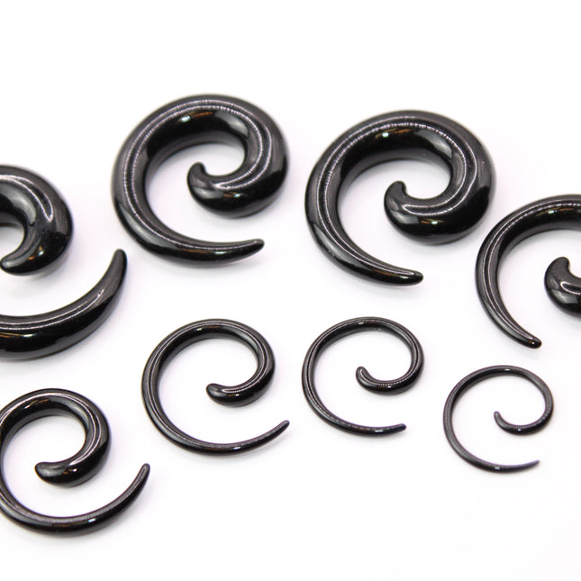 A pair of sleek, black acrylic spiral taper earrings displayed on a clean, neutral surface. The spirals curve smoothly in a bold, symmetrical design, tapering to fine points at the ends. Their glossy finish reflects light subtly, emphasizing their smooth texture and modern, minimalist style. Sized for stretched ears, the earrings showcase a striking balance of simplicity and statement, perfect for alternative or gauged jewelry wearers.