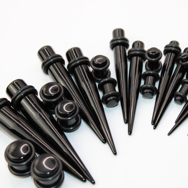 A complete ear stretching kit displayed in size order, featuring black acrylic tapers and matching double flare plugs. The tapers are sleek and lightweight, gradually increasing in size from 14G to 00G, designed to assist with smooth and safe ear stretching. Each size comes with a pair of straight tapers and a matching pair of plugs, all with rounded edges and rubber O-rings for secure placement. The set is neatly arranged to show the full gauge progression, ideal for beginne
