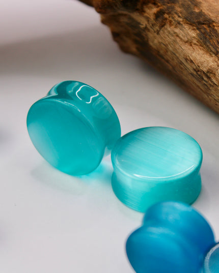 A vibrant pair of Pink Cat's Eye glass plugs, featuring a smooth double flare design for a snug, comfortable fit. These plugs showcase a radiant pink color with a captivating cat’s eye effect—a luminous, shifting line that moves with the light, giving the glass a glowing, almost fiber-optic appearance. Polished to a high shine, the surface enhances the soft, elegant hue while adding a playful yet sophisticated touch.