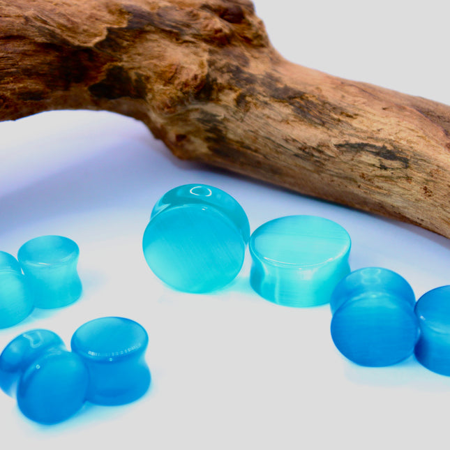 A vibrant pair of Pink Cat's Eye glass plugs, featuring a smooth double flare design for a snug, comfortable fit. These plugs showcase a radiant pink color with a captivating cat’s eye effect—a luminous, shifting line that moves with the light, giving the glass a glowing, almost fiber-optic appearance. Polished to a high shine, the surface enhances the soft, elegant hue while adding a playful yet sophisticated touch.