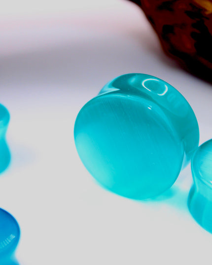 A vibrant pair of Pink Cat's Eye glass plugs, featuring a smooth double flare design for a snug, comfortable fit. These plugs showcase a radiant pink color with a captivating cat’s eye effect—a luminous, shifting line that moves with the light, giving the glass a glowing, almost fiber-optic appearance. Polished to a high shine, the surface enhances the soft, elegant hue while adding a playful yet sophisticated touch.
