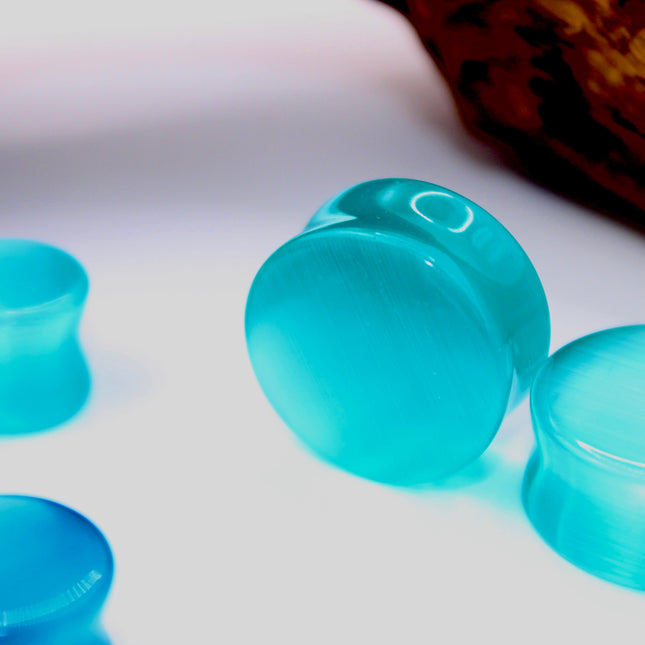 A vibrant pair of Pink Cat's Eye glass plugs, featuring a smooth double flare design for a snug, comfortable fit. These plugs showcase a radiant pink color with a captivating cat’s eye effect—a luminous, shifting line that moves with the light, giving the glass a glowing, almost fiber-optic appearance. Polished to a high shine, the surface enhances the soft, elegant hue while adding a playful yet sophisticated touch.