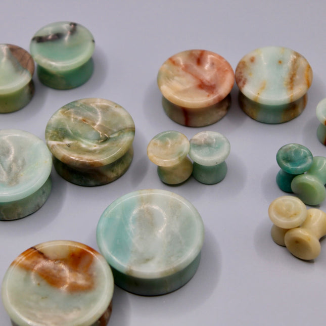 A beautiful pair of Natural Calcite stone plugs, hand-carved and polished into a smooth double flare shape for a secure and comfortable fit. These ear gauges showcase the soft, luminous quality of calcite, with creamy whites, warm honey tones, and subtle translucency that varies from piece to piece. Each plug highlights unique natural banding and organic patterns, making every pair one-of-a-kind.