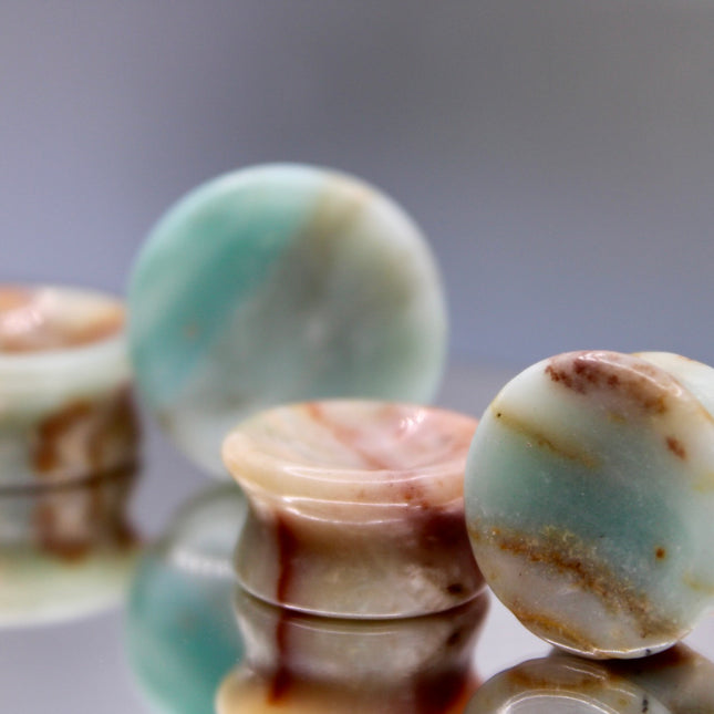 A beautiful pair of Natural Calcite stone plugs, hand-carved and polished into a smooth double flare shape for a secure and comfortable fit. These ear gauges showcase the soft, luminous quality of calcite, with creamy whites, warm honey tones, and subtle translucency that varies from piece to piece. Each plug highlights unique natural banding and organic patterns, making every pair one-of-a-kind.