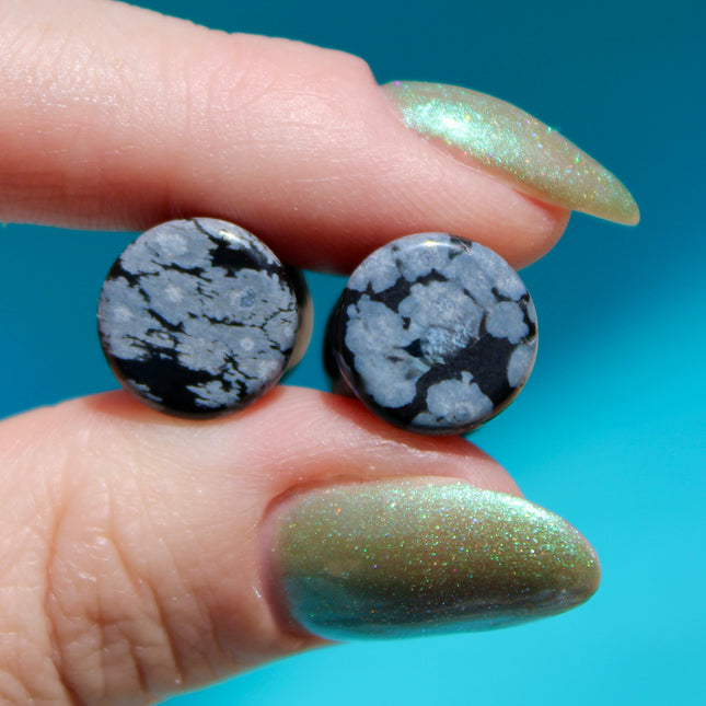 These Snowflake Obsidian Double Flared Plugs feature a smooth, polished surface with natural gray-white crystal "snowflakes" scattered across a rich black volcanic glass base. The double flare ensures a secure, comfortable fit for stretched ears without the need for O-rings. Each pair is uniquely patterned, showcasing the stone’s natural beauty and grounding energy. Durable and stylish, these plugs add a bold yet refined touch to any stretched ear jewelry collection.