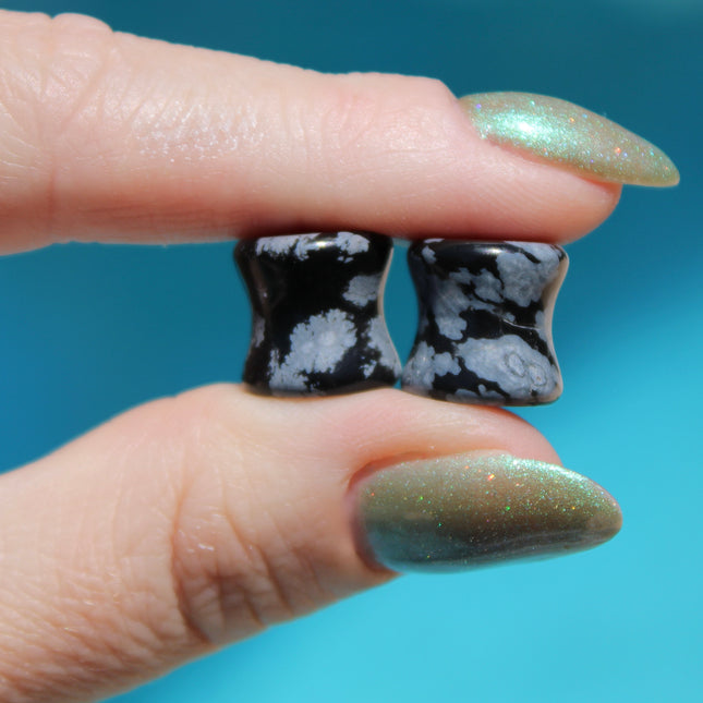 These Snowflake Obsidian Double Flared Plugs feature a smooth, polished surface with natural gray-white crystal "snowflakes" scattered across a rich black volcanic glass base. The double flare ensures a secure, comfortable fit for stretched ears without the need for O-rings. Each pair is uniquely patterned, showcasing the stone’s natural beauty and grounding energy. Durable and stylish, these plugs add a bold yet refined touch to any stretched ear jewelry collection.