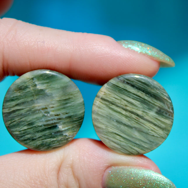 A bold pair of Green Jasper Double Flare Plugs sits elegantly on a neutral surface, radiating natural strength and earthy charm. Each plug is carved from genuine Green Jasper, showcasing deep olive and forest tones, marbled with organic patterns of black, brown, or mossy veining. The polished surface highlights the stone’s natural texture and depth, making every pair unique.