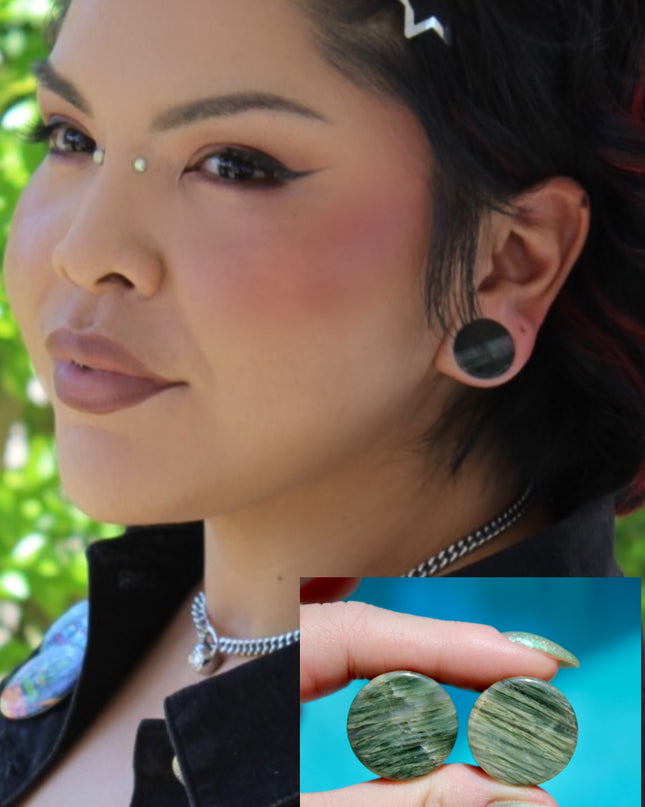 A bold pair of Green Jasper Double Flare Plugs sits elegantly on a neutral surface, radiating natural strength and earthy charm. Each plug is carved from genuine Green Jasper, showcasing deep olive and forest tones, marbled with organic patterns of black, brown, or mossy veining. The polished surface highlights the stone’s natural texture and depth, making every pair unique. 