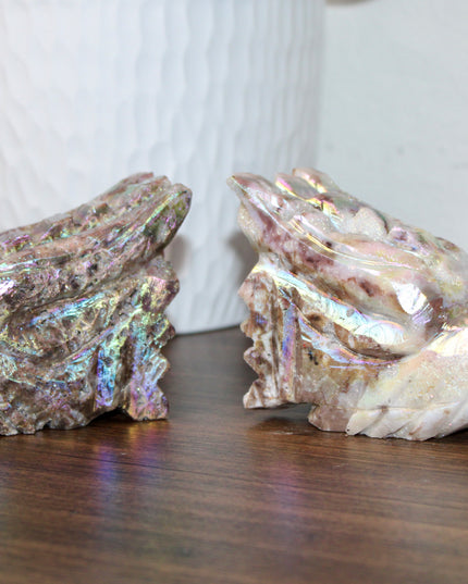 Person holding a large, iridescent dragon skull crystal carving with a blurred green plant background