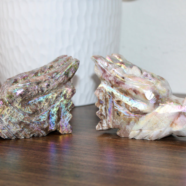 Person holding a large, iridescent dragon skull crystal carving with a blurred green plant background
