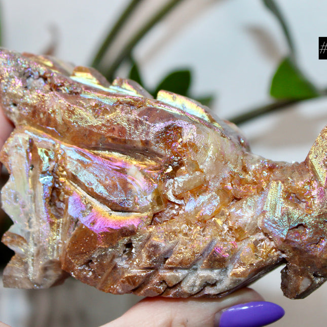 Person holding a large, iridescent dragon skull crystal carving with a blurred green plant background