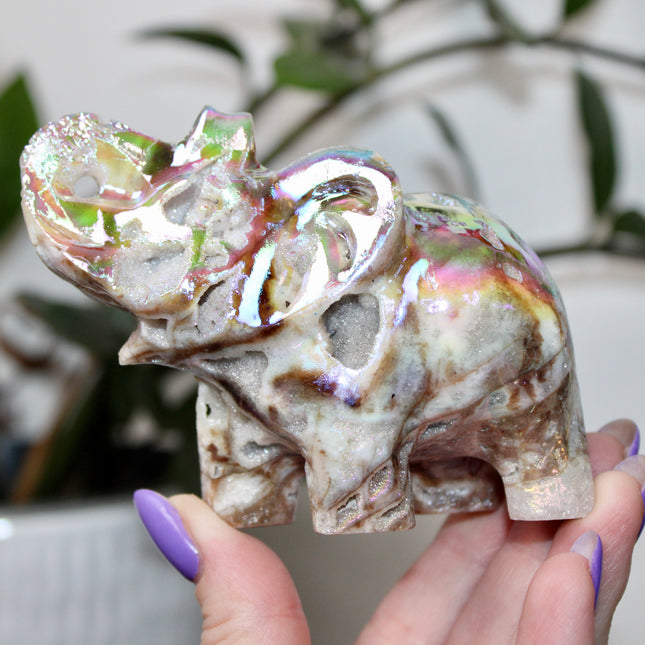This Aura Quartz Elephant Carving features a charming hand-carved design enhanced with a brilliant rainbow electroplated finish. Made from natural quartz and treated to produce a luminous, color-shifting surface, this figurine blends natural beauty with a playful, eye-catching twist.