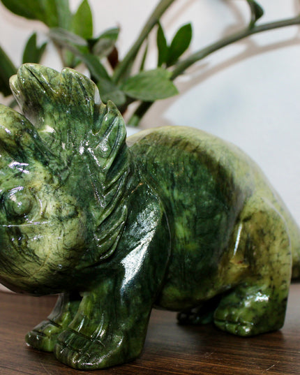 Green stone triceratops figurine on a wooden surface with plants in the background