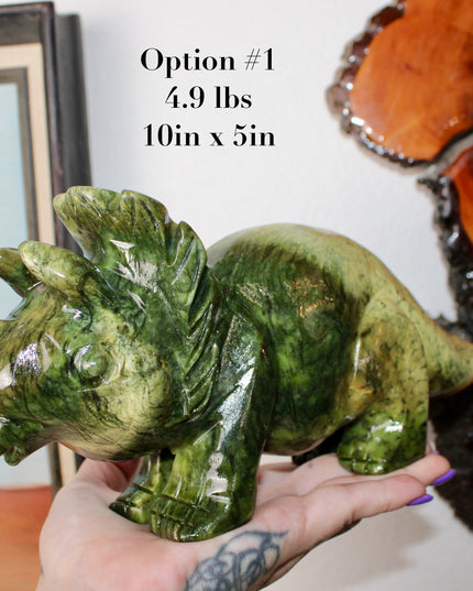 Green stone triceratops figurine on a wooden surface with plants in the background