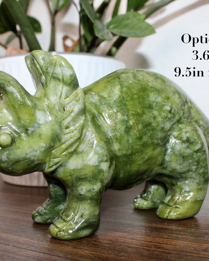 Green stone triceratops figurine on a wooden surface with plants in the background