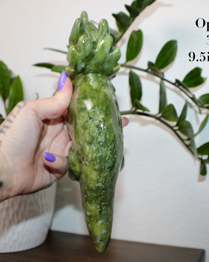 Green stone triceratops figurine on a wooden surface with plants in the background