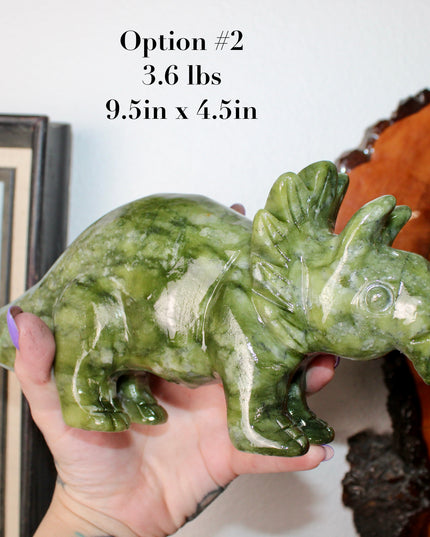 Green stone triceratops figurine on a wooden surface with plants in the background