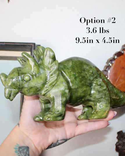 Green stone triceratops figurine on a wooden surface with plants in the background