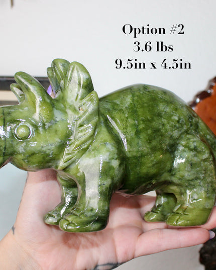 Green stone triceratops figurine on a wooden surface with plants in the background