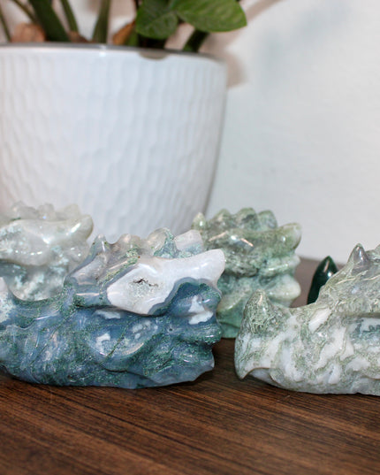 Bring a sense of majestic artistry and natural wonder into your space with this hand‑carved moss agate dragon skull. Sculpted from a single piece of genuine moss agate celebrated for its swirling green “moss-like” inclusions set against milky chalcedony, each piece showcases its own unique, earthy landscape