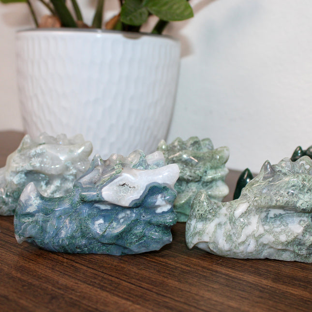 Bring a sense of majestic artistry and natural wonder into your space with this hand‑carved moss agate dragon skull. Sculpted from a single piece of genuine moss agate celebrated for its swirling green “moss-like” inclusions set against milky chalcedony, each piece showcases its own unique, earthy landscape