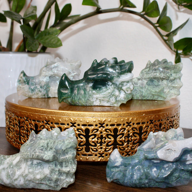 Bring a sense of majestic artistry and natural wonder into your space with this hand‑carved moss agate dragon skull. Sculpted from a single piece of genuine moss agate celebrated for its swirling green “moss-like” inclusions set against milky chalcedony, each piece showcases its own unique, earthy landscape