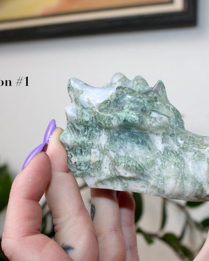 Bring a sense of majestic artistry and natural wonder into your space with this hand‑carved moss agate dragon skull. Sculpted from a single piece of genuine moss agate celebrated for its swirling green “moss-like” inclusions set against milky chalcedony, each piece showcases its own unique, earthy landscape