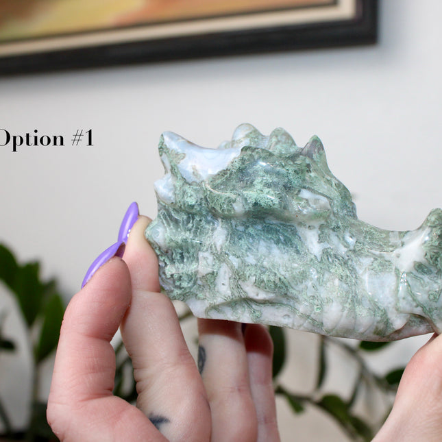 Bring a sense of majestic artistry and natural wonder into your space with this hand‑carved moss agate dragon skull. Sculpted from a single piece of genuine moss agate celebrated for its swirling green “moss-like” inclusions set against milky chalcedony, each piece showcases its own unique, earthy landscape