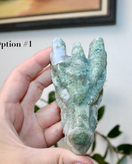 Bring a sense of majestic artistry and natural wonder into your space with this hand‑carved moss agate dragon skull. Sculpted from a single piece of genuine moss agate celebrated for its swirling green “moss-like” inclusions set against milky chalcedony, each piece showcases its own unique, earthy landscape