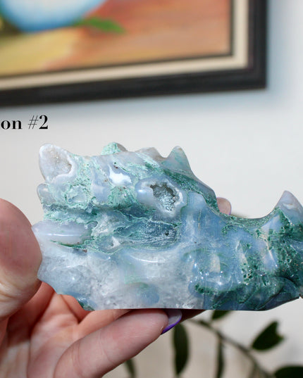 Bring a sense of majestic artistry and natural wonder into your space with this hand‑carved moss agate dragon skull. Sculpted from a single piece of genuine moss agate celebrated for its swirling green “moss-like” inclusions set against milky chalcedony, each piece showcases its own unique, earthy landscape
