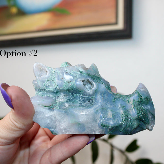 Bring a sense of majestic artistry and natural wonder into your space with this hand‑carved moss agate dragon skull. Sculpted from a single piece of genuine moss agate celebrated for its swirling green “moss-like” inclusions set against milky chalcedony, each piece showcases its own unique, earthy landscape