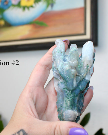 Bring a sense of majestic artistry and natural wonder into your space with this hand‑carved moss agate dragon skull. Sculpted from a single piece of genuine moss agate celebrated for its swirling green “moss-like” inclusions set against milky chalcedony, each piece showcases its own unique, earthy landscape