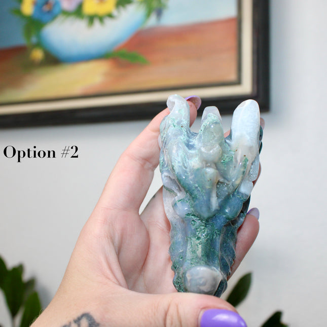 Bring a sense of majestic artistry and natural wonder into your space with this hand‑carved moss agate dragon skull. Sculpted from a single piece of genuine moss agate celebrated for its swirling green “moss-like” inclusions set against milky chalcedony, each piece showcases its own unique, earthy landscape