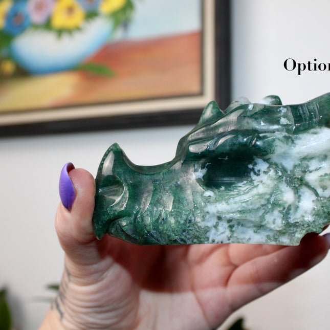 Bring a sense of majestic artistry and natural wonder into your space with this hand‑carved moss agate dragon skull. Sculpted from a single piece of genuine moss agate celebrated for its swirling green “moss-like” inclusions set against milky chalcedony, each piece showcases its own unique, earthy landscape