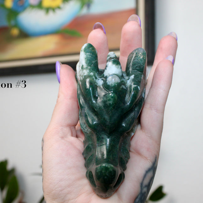 Bring a sense of majestic artistry and natural wonder into your space with this hand‑carved moss agate dragon skull. Sculpted from a single piece of genuine moss agate celebrated for its swirling green “moss-like” inclusions set against milky chalcedony, each piece showcases its own unique, earthy landscape