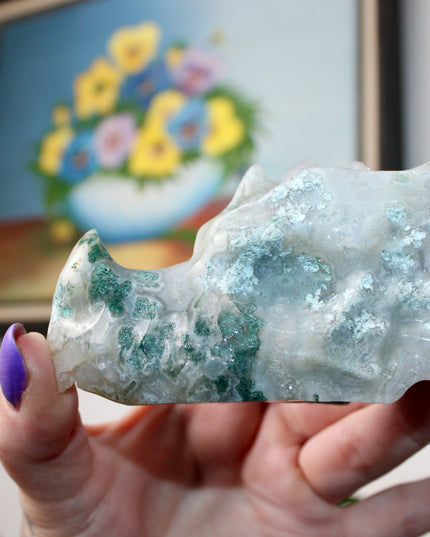 Bring a sense of majestic artistry and natural wonder into your space with this hand‑carved moss agate dragon skull. Sculpted from a single piece of genuine moss agate celebrated for its swirling green “moss-like” inclusions set against milky chalcedony, each piece showcases its own unique, earthy landscape