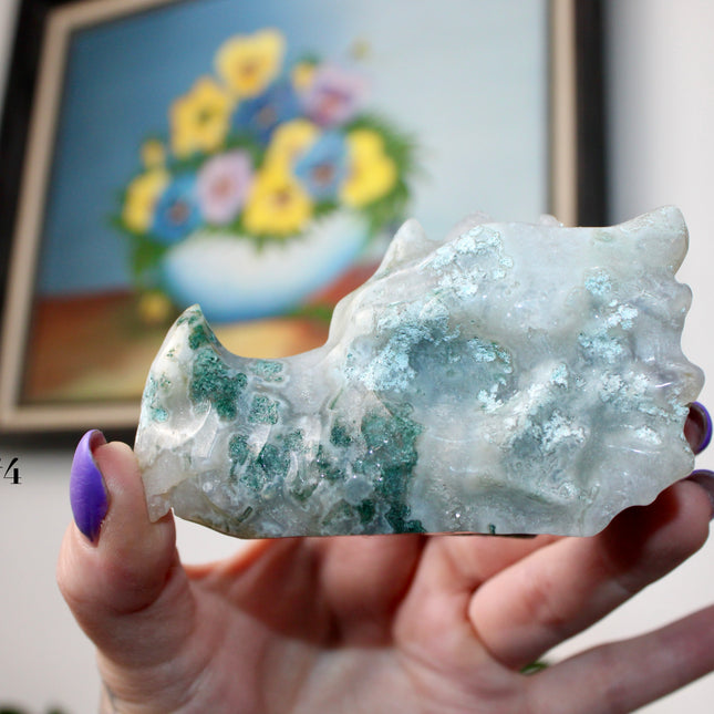 Bring a sense of majestic artistry and natural wonder into your space with this hand‑carved moss agate dragon skull. Sculpted from a single piece of genuine moss agate celebrated for its swirling green “moss-like” inclusions set against milky chalcedony, each piece showcases its own unique, earthy landscape