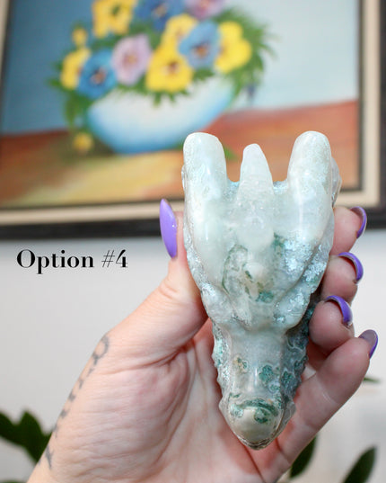 Bring a sense of majestic artistry and natural wonder into your space with this hand‑carved moss agate dragon skull. Sculpted from a single piece of genuine moss agate celebrated for its swirling green “moss-like” inclusions set against milky chalcedony, each piece showcases its own unique, earthy landscape