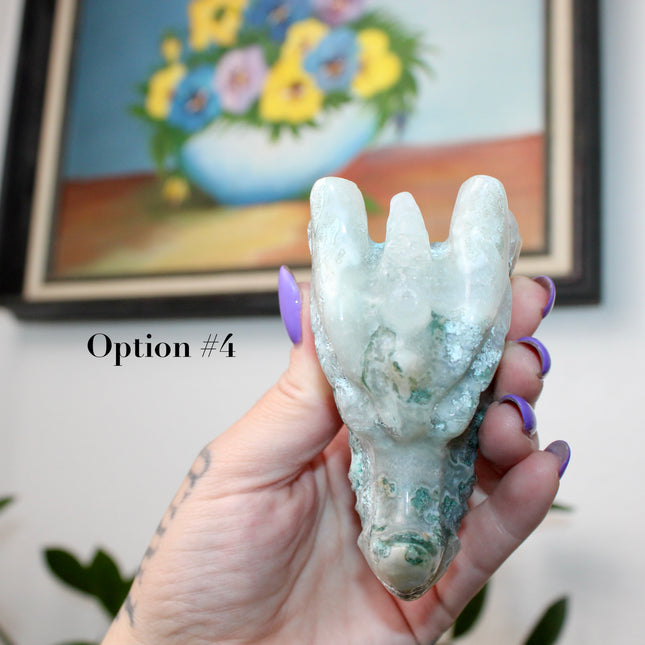 Bring a sense of majestic artistry and natural wonder into your space with this hand‑carved moss agate dragon skull. Sculpted from a single piece of genuine moss agate celebrated for its swirling green “moss-like” inclusions set against milky chalcedony, each piece showcases its own unique, earthy landscape