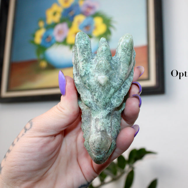Bring a sense of majestic artistry and natural wonder into your space with this hand‑carved moss agate dragon skull. Sculpted from a single piece of genuine moss agate celebrated for its swirling green “moss-like” inclusions set against milky chalcedony, each piece showcases its own unique, earthy landscape