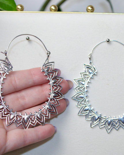 Silver hoop gauge earring with intricate Indian mandala design held in a hand against a plain background