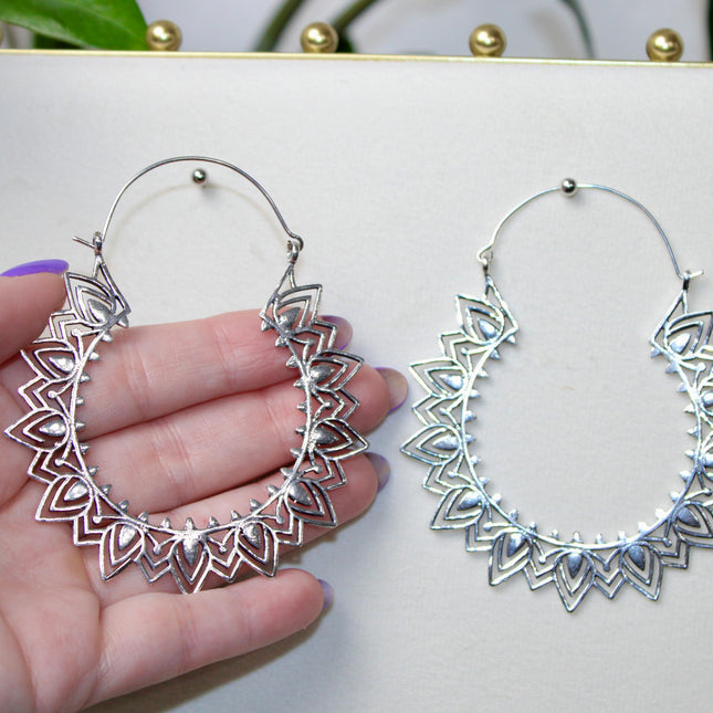 Silver hoop gauge earring with intricate Indian mandala design held in a hand against a plain background