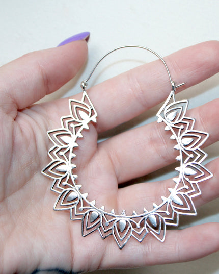 Silver hoop gauge earring with intricate Indian mandala design held in a hand against a plain background