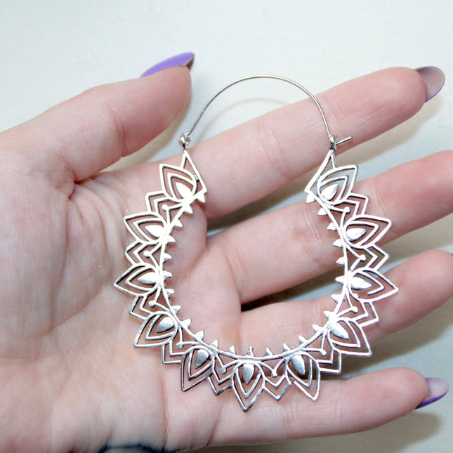 Silver hoop gauge earring with intricate Indian mandala design held in a hand against a plain background