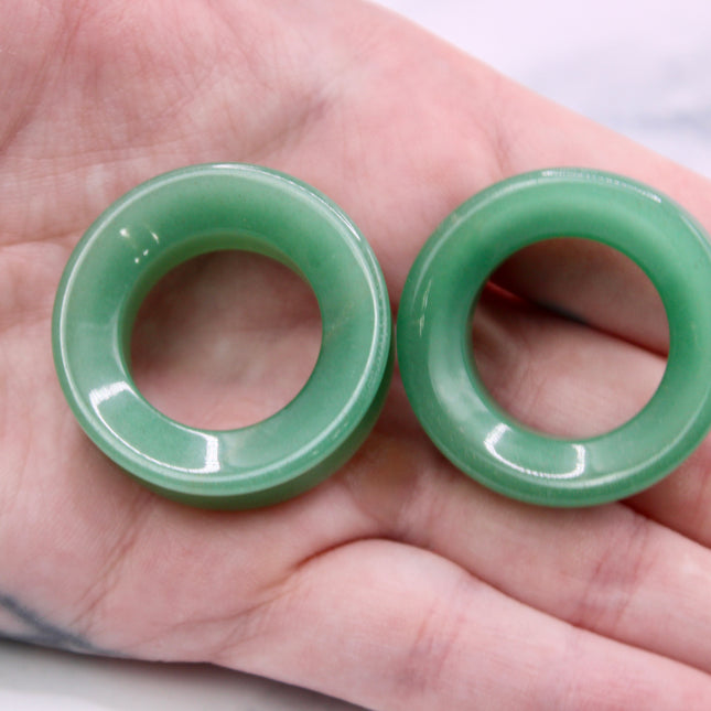 Two green jade tunnel plugs held in a hand against a neutral background