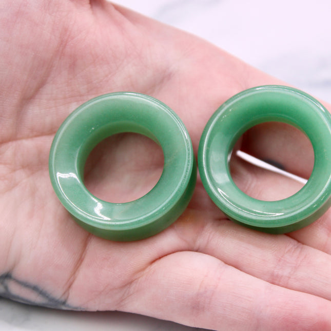 Two green jade tunnel plugs held in a hand against a white background