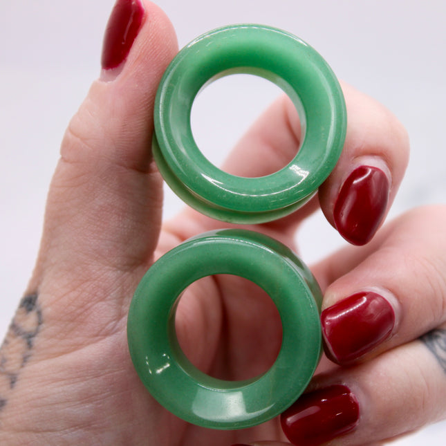 Green tunnel plugs jade green aventurine held in a hand with red nail polish on a white background