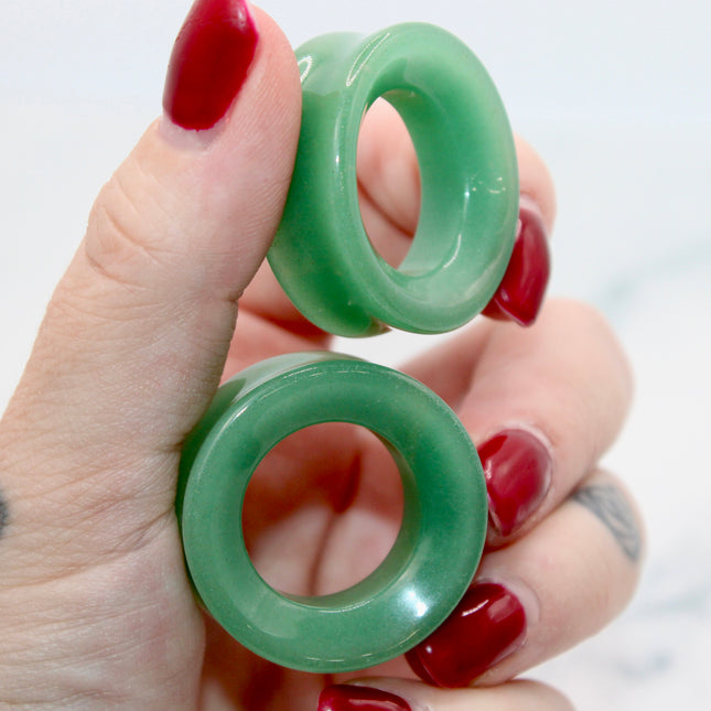 Green jade tunnel plugs held by a hand with red nail polish on a white background